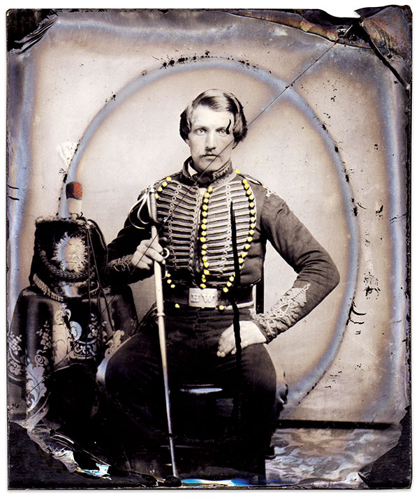 This trooper of the 3rd Regiment (Hussars), New York State Militia, above, wears the uniform adopted by the regiment in 1854. Minus the pelisse, the uniform consisted of a blue hussar jacket trimmed with gold and yellow worsted cord and lace, and dark blue pantaloons with a wide yellow outer seam. His Prussian-style cap features a visor, black fur body, scarlet cloth bag trimmed with yellow hanging down the side, and red and white worsted pompon. Having an upright spread eagle set within a starburst, the plate on his cap is of the pattern worn with the 1833 U.S. dragoon cap. His waist belt has the letters WH—the Washington Hussars, Troop E. He holds a Model 1840 Dragoon saber of the pattern retailed by Horstmann & Sons of Philadelphia. Other arms and equipage carried by each man in his regiment consisted of two “improved horse pistols” in saddle holsters and black belts with “neat cartridge boxes.” Sixth plate ambrotype by an unidentified photographer. Jérôme Lantz Collection.