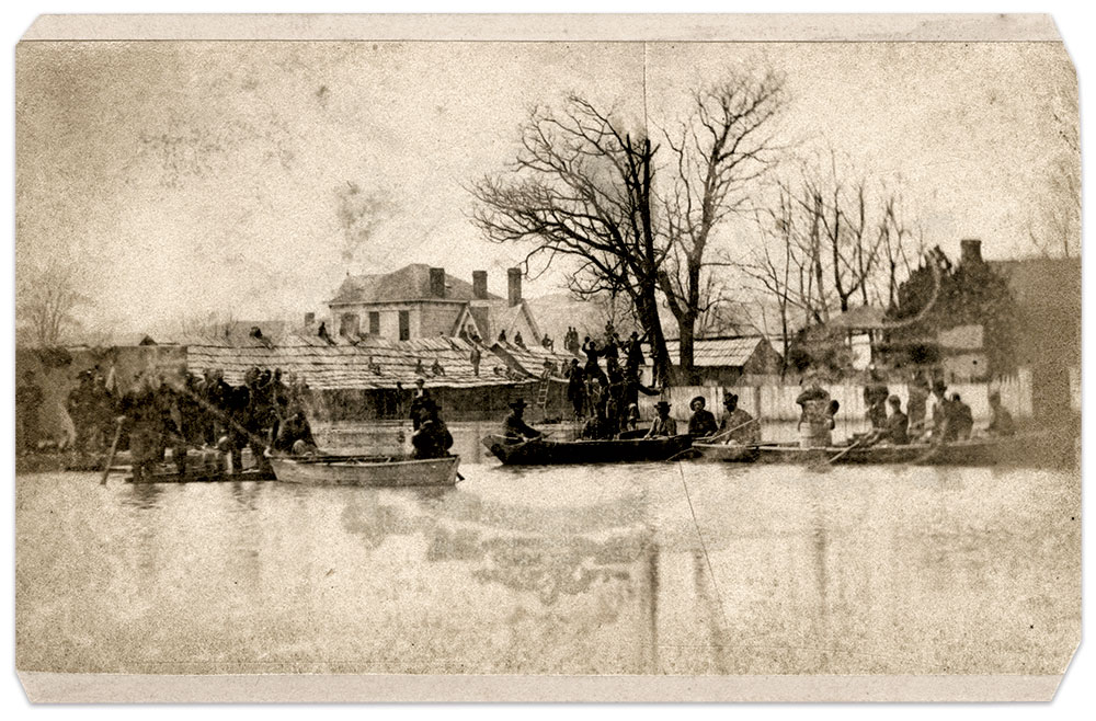 Soldiers row through the streets of Helena in this scene from the 1865 flood. The house with columns was occupied by the Matron of the Industrial School established by the Freedman’s Bureau. To the left of the residence are barracks occupied by two companies of the 56th U.S. Colored Infantry. Butler Center for Arkansas Studies.