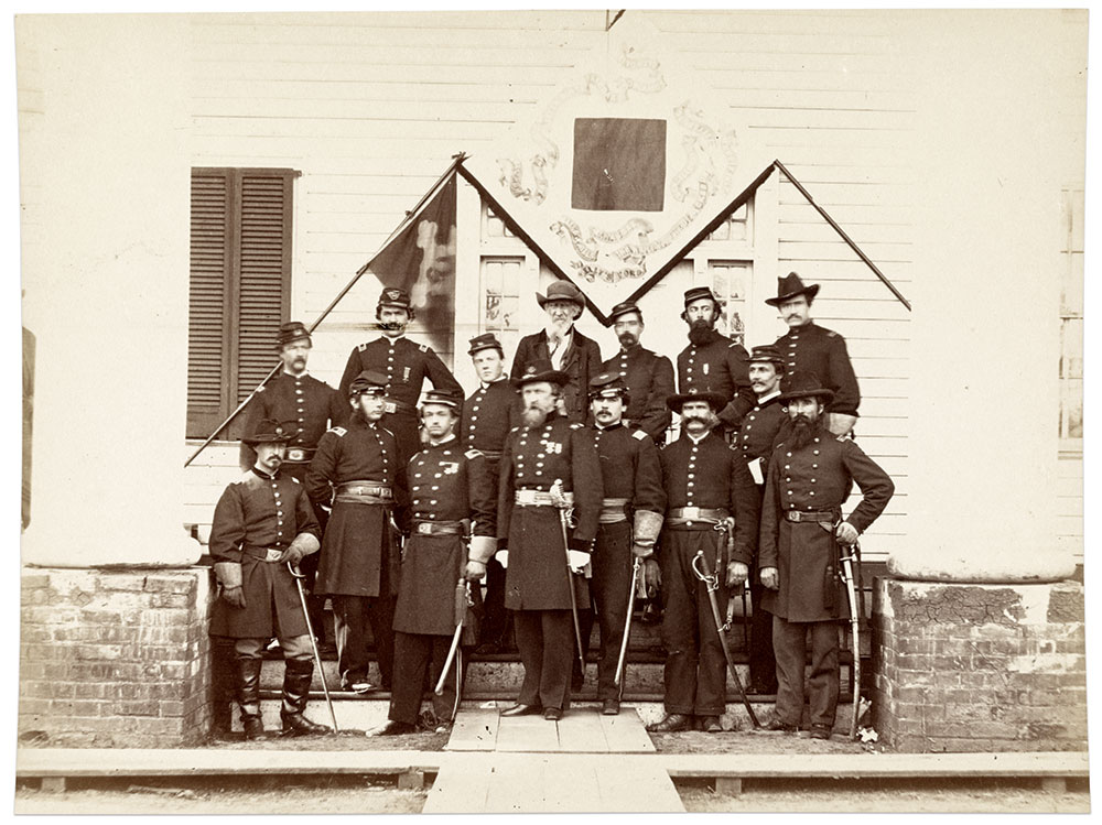 Birney and his staff, including Fassett standing below the bottom corner of a Third Corps flag, at Brandy Station, Va., on Feb. 17, 1864. The civilian next to Fassett, named Rixey, is likely a member of the prominent family in nearby Culpeper. Albumen print by Alexander Gardner of Washington, D.C. Library of Congress.