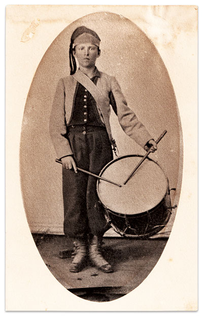 Levi Carlton “Lee” Thayer (1845-1923) enlisted as a drummer in the City Grays, which became Company A of Wallace’s Zouaves in August 1861. He wears the musician’s version of the first uniform issued to his regiment consisting of a red-trimmed gray jacket, but with the addition of a fez with gray pointed band and darker top and tassel, which was likely red, and pantaloons which were also likely red. Present at the battles of Fort Donelson and Shiloh, Thayer received a discharge at Pittsburg Landing on account of “he not being a musician.” Returning to his home in Hancock County, Ind., he became a locomotive engineer. Circa 1920s copy print of a Civil War-period photograph. Dan Miller Collection.